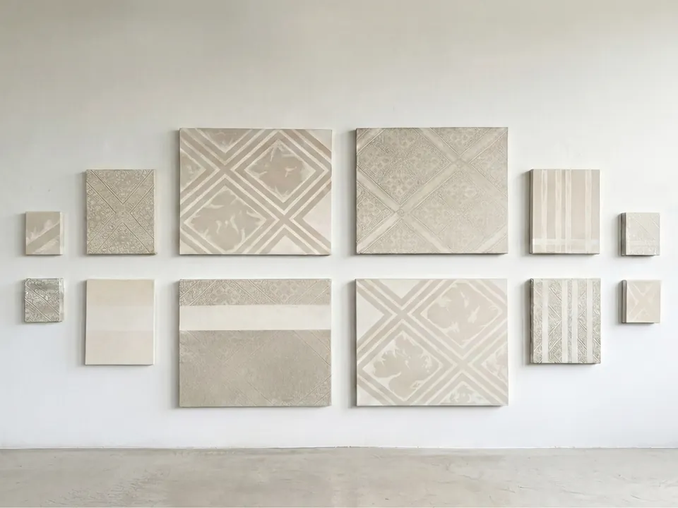 Vue d’installation : douze tableaux de tailles variées, en tissu Tarz et en toile brute, accrochés en deux rangées symétriques sur un mur blanc.